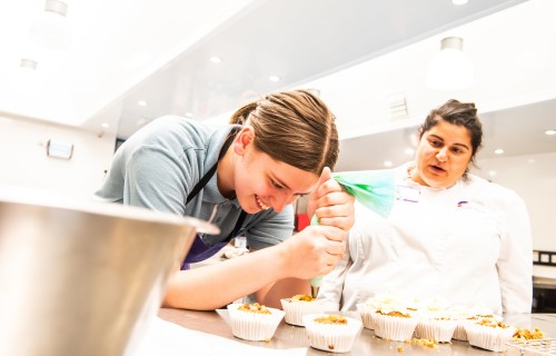 Cook helping student to decorate cupcakes
