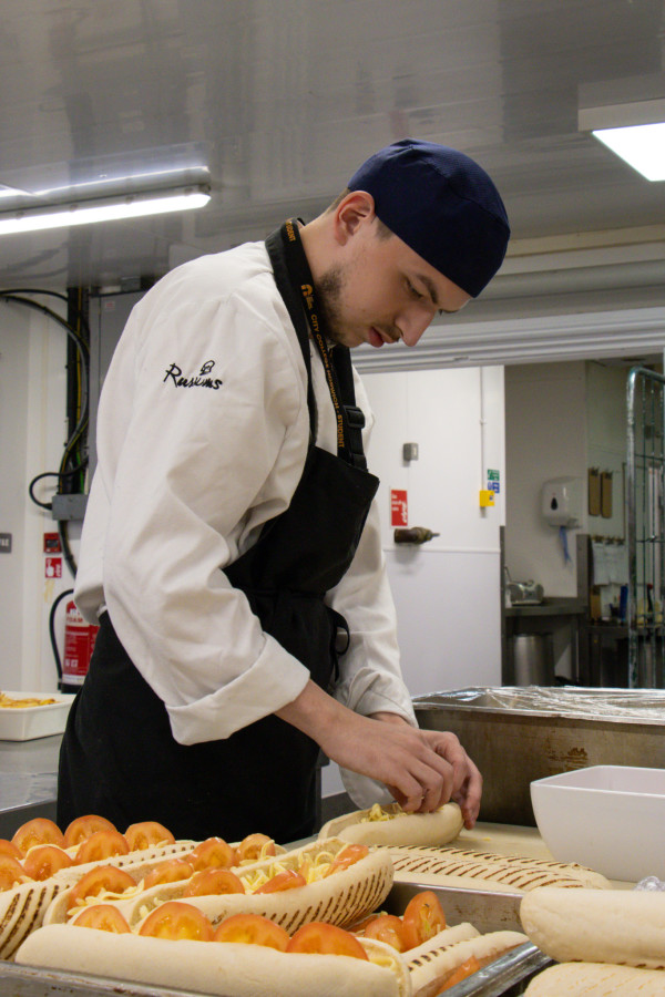 A student in chef whites putting together cheese and tomato paninis.