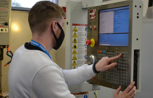 Student wearing a mask uses a control panel in a workshop